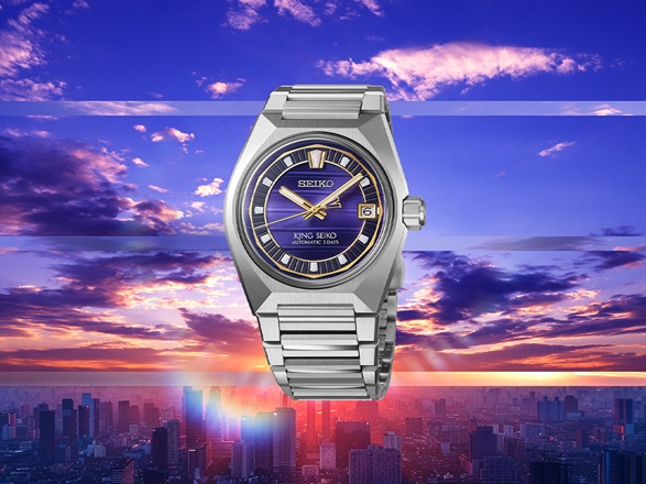 Imagem de relógio King Seiko prateado sobre fundo cinza com emblema King Seiko esbatido em segundo plano.